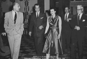 A smiling man and woman in formal clothes walk together into an awards ceremony, with three men in suits standing nearby.